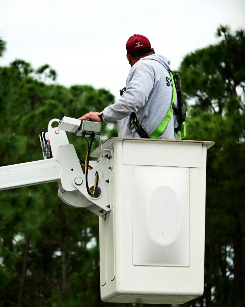 A worker with safety gear operates a bucket truck outside, emphasizing safety and skill.